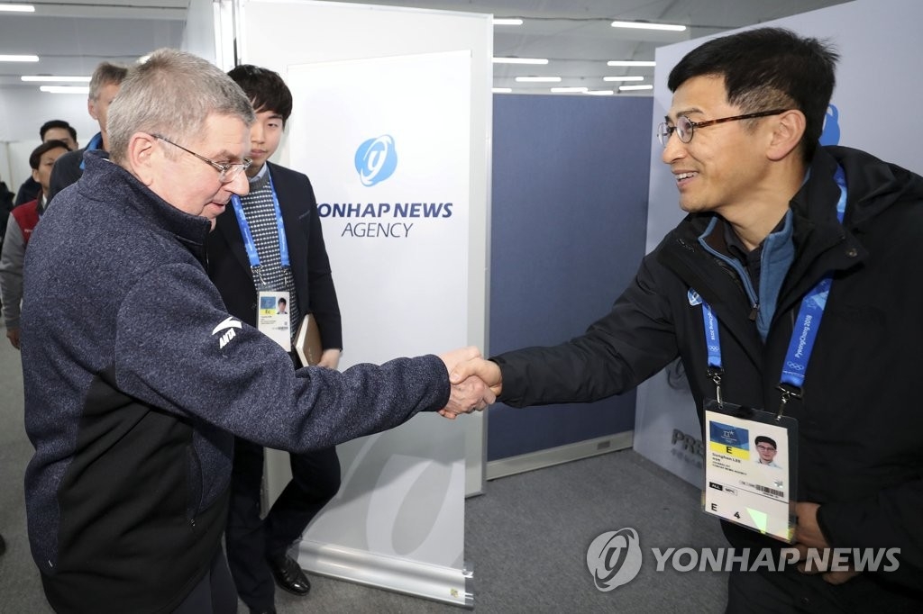 2月12日下午,在江原道平昌冬奧新聞中心,巴赫(左)訪問韓聯社的採訪區並同韓聯社冬奧採訪工作總負責人李盛漢握手。(韓聯社)