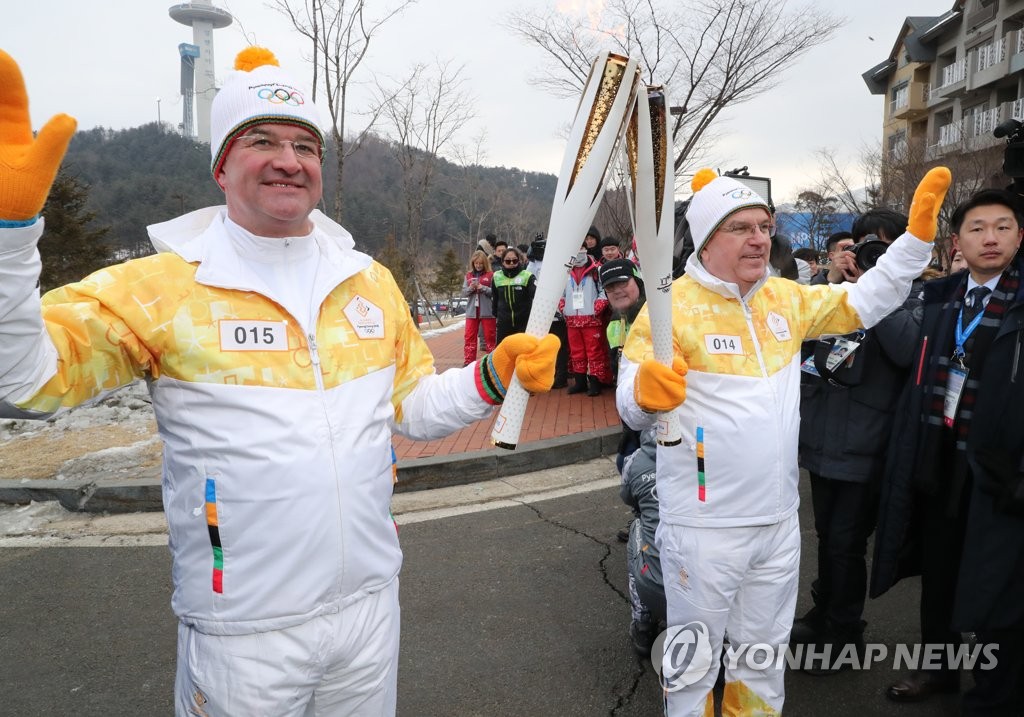 2月9日上午,在平昌阿爾卑西亞度假村附近,巴赫(右)把火炬交接給米羅斯拉伕·萊恰克。(韓聯社)